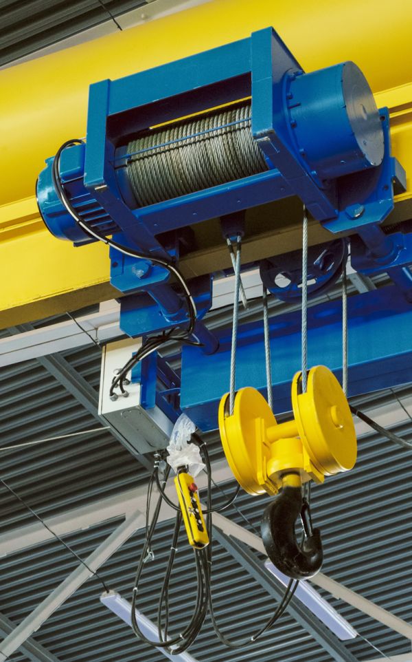 Industrieller Laufkran mit blau-gelbem Hubwerk und Steuerungskabel